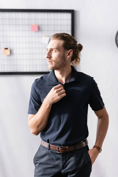 Confident businessman with hand in pocket looking away while standing in office with blurred mesh organizer on background - Photo, Image