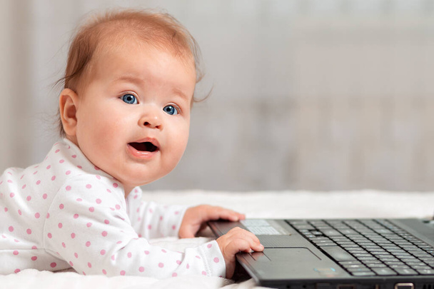 Portret szczęśliwego dziecka leży na łóżku i trzyma się laptopa rękami. Odbiór. Koncepcja rozrywki i edukacji dla dzieci korzystających z Internetu. - Zdjęcie, obraz