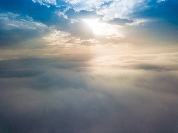 Vuelo aéreo con drones sobre la niebla. Hay densas nubes de niebla abajo, el sol rompe las nubes. - Foto, Imagen