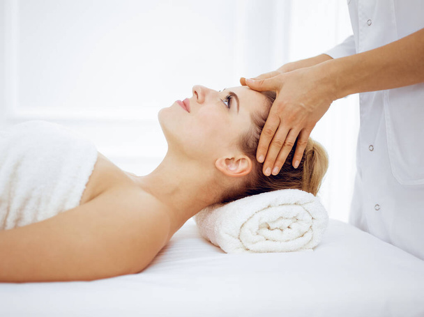 Young and blonde woman enjoying facial massage in spa salon. Beauty concept - Fotografie, Obrázek