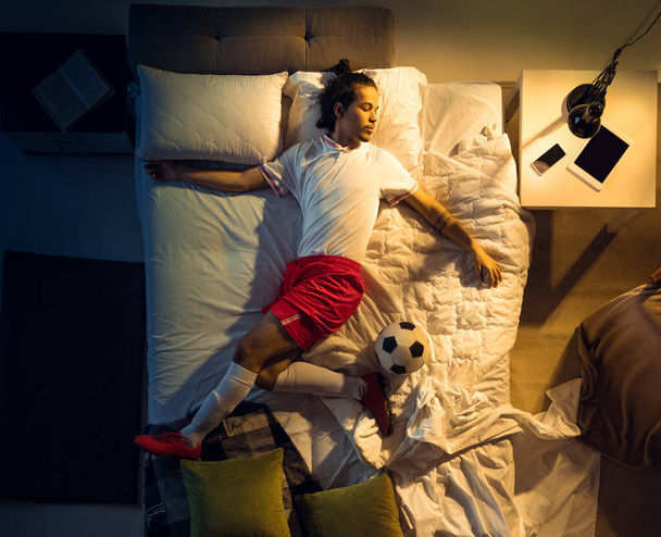 Top view of young professional football, soccer player sleeping at his bedroom in sportwear with ball - Фото, зображення