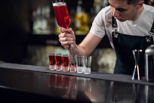o barman enche tiros com licor vermelho de uma garrafa no bar - Foto, Imagem