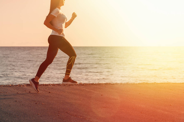 スポーツや海に沿ってジョギング。若いブルネットの女性が海岸沿いの道を走っています。背景には、夕日の海と空。スペースを閉じてコピーする. - 写真・画像