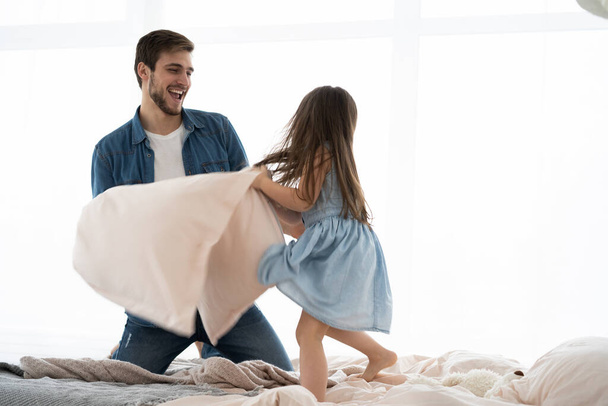 happy father and daughter playing pillow fight in bed at morning - Zdjęcie, obraz