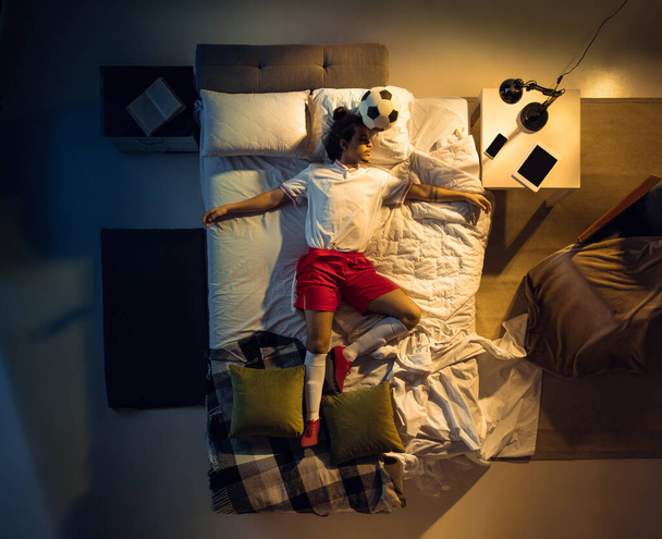 若いプロサッカーのトップビュー,サッカー選手はボールとスポーツウェアで彼の寝室で寝て - 写真・画像