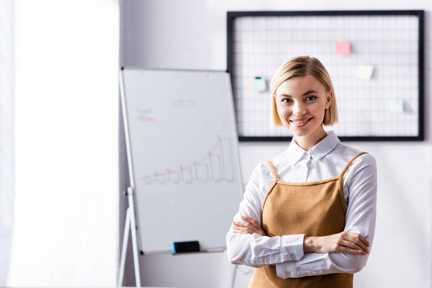 happy, blonde businesswoman looking at camera while standing with crossed arms - Photo, Image