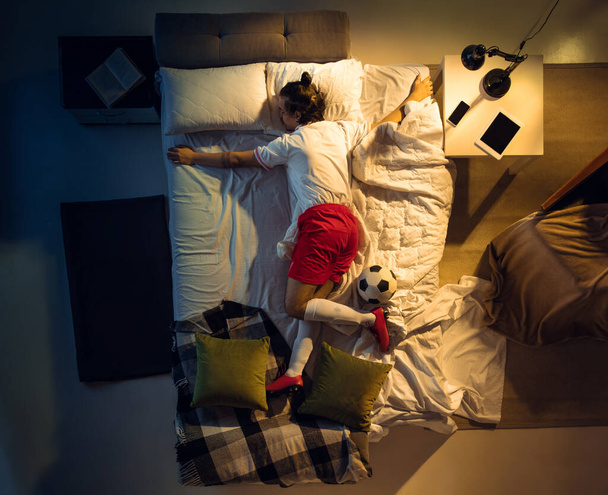 Top view of young professional football, soccer player sleeping at his bedroom in sportwear with ball - Foto, Bild