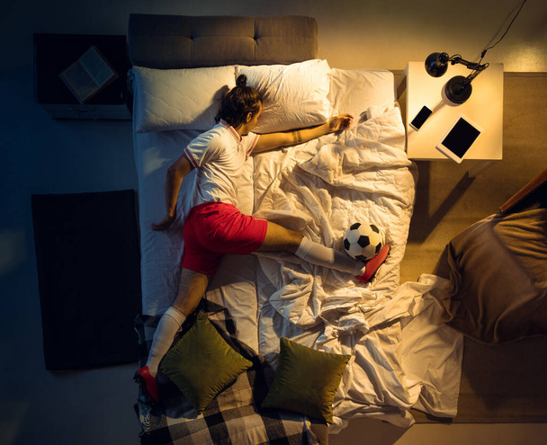 Top view of young professional football, soccer player sleeping at his bedroom in sportwear with ball - Photo, image