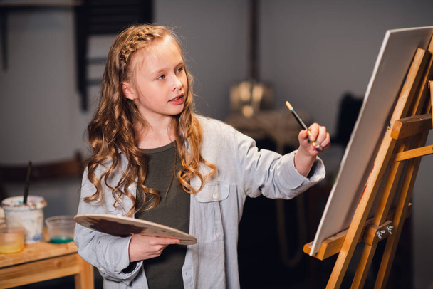 Jong meisje creatief kunstenaar aan het werk in een workshop. Met passie tekent een beeld ondergedompeld in werk. - Foto, afbeelding