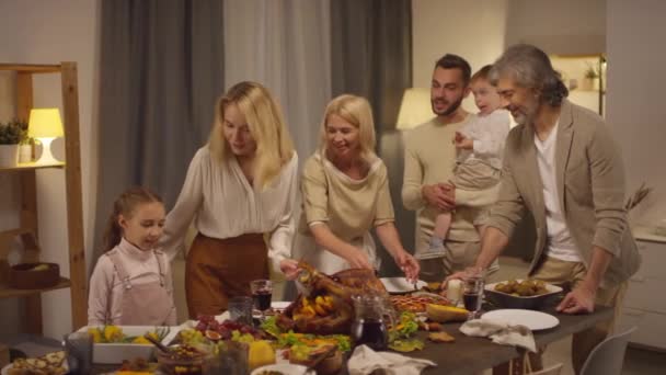 Szczęśliwa duża rodzina z dziećmi spędzającymi razem wieczór Dziękczynienia zbierając się przy stole jadalnym, średnim ujęciu - Materiał filmowy, wideo