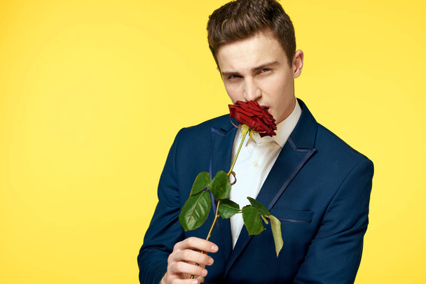 Young man in a classic suit with a red rose in his hand on a yellow background emotions cropped view model - Valokuva, kuva