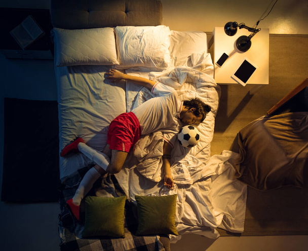 Top view of young professional football, soccer player sleeping at his bedroom in sportwear with ball - Фото, изображение