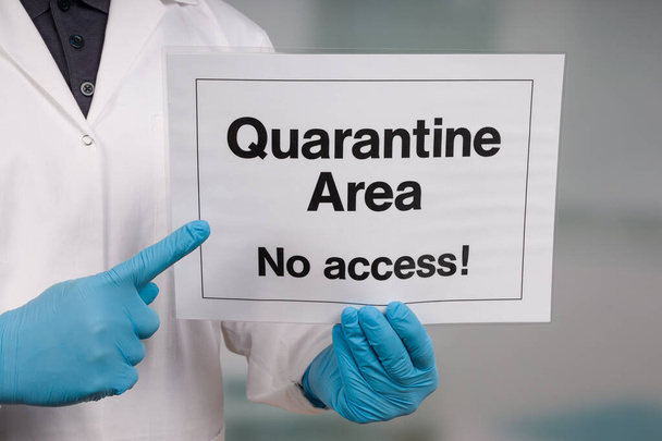 Doctor's hand in medical gloves pointing to a quarantine sign in front of a clinic room - Фото, изображение