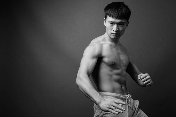 Studio shot of young Chinese man shirtless against gray background in black and white - Foto, imagen