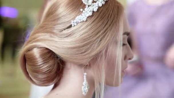 Uma bela noiva jovem com um penteado elegante, um diadema na cabeça e brincos olha para si mesma no espelho - Filmagem, Vídeo
