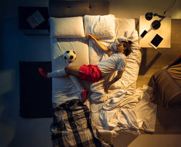 Top view of young professional football, soccer player sleeping at his bedroom in sportwear with ball - Photo, Image