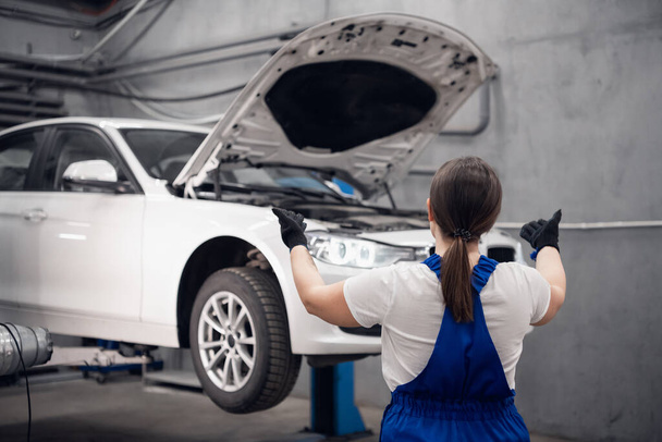働く女性はガレージのリフトを使用して車を持ち上げる - 写真・画像