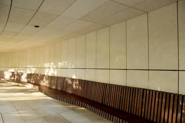 Un banc en bois avec un dossier est installé le long du mur de marbre. La lumière tombe sur un banc dans un passage de pierre. - Photo, image