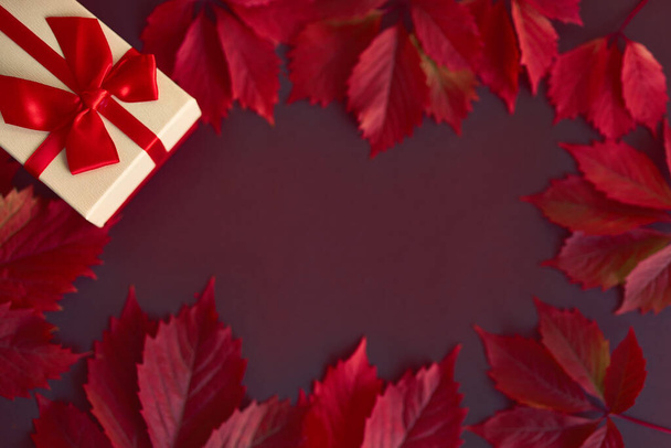 Karácsonyi doboz piros szalaggal és vörös őszi levelekkel - Fotó, kép