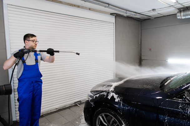 Worker cleaning automobile with high pressure water jet at car wash. - Foto, afbeelding