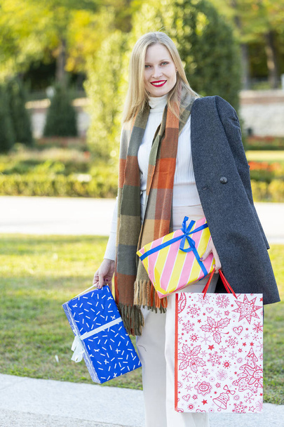Noel sokaklara dökülür, hediyeler, alışveriş çantaları ve Noel süsleriyle genç bir kadın. - Fotoğraf, Görsel