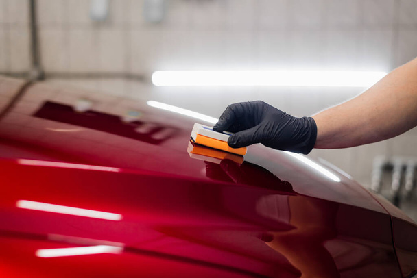 Працівник автомобіля деталізує студію нанесення керамічного покриття на автомобільну фарбу з аплікатором губки
 - Фото, зображення