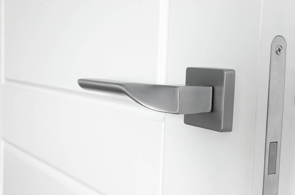 The silver metal doorknob is mounted in a white wooden door. Repair - Zdjęcie, obraz