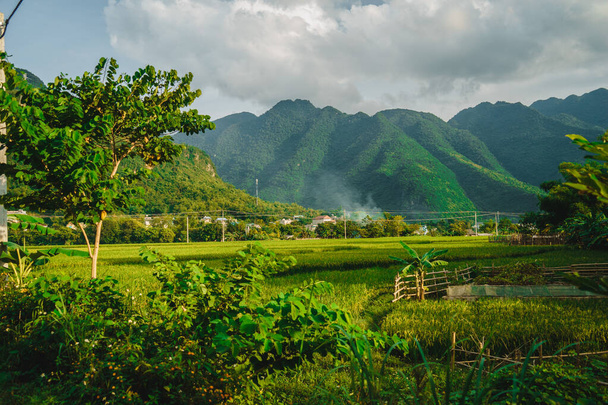 A cluster of home stay and local houses on a hillside between a green rice field and mountains, Mai Chau Valley, Vietnam, Southeast Asia. Travel and nature concept. - Photo, image