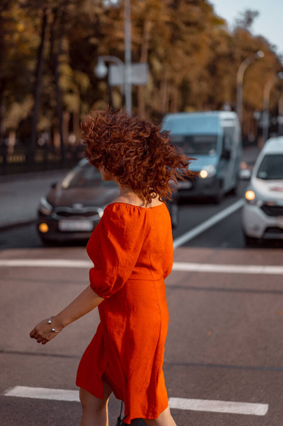 A beautiful woman in a red dress walks around the city on an autumn day. - Zdjęcie, obraz