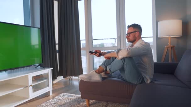 Hombre en casa acostado en un sofá y viendo la televisión con pantalla verde simulada - Imágenes, Vídeo