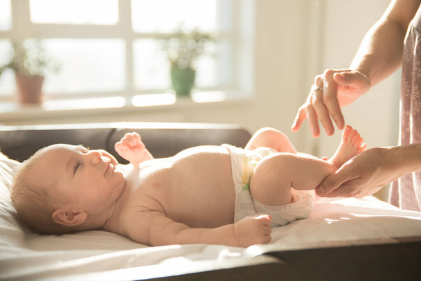 母マッサージ足の彼女の小さな笑みを浮かべて赤ん坊のベッドの上に横たわる - 写真・画像
