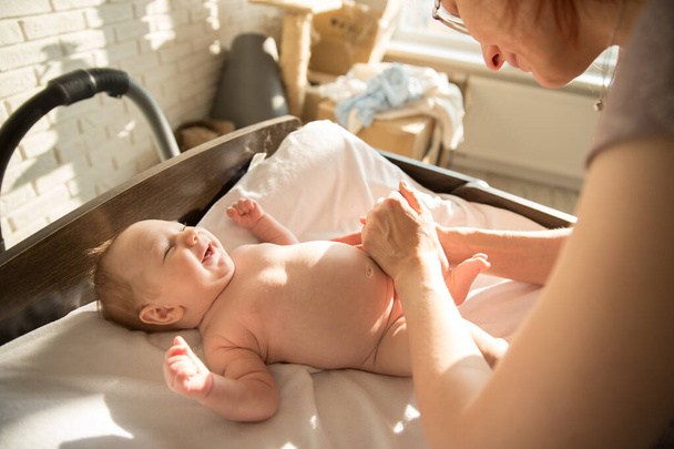 Madre masajeando las piernas de su bebé sonriente acostado en una cama - Foto, Imagen