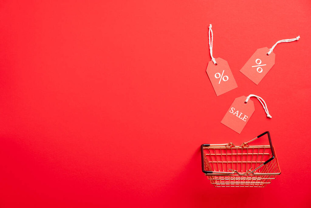 Shopping basket and tags on red background. Black Friday Sale concept. Flat lay, top view. - Valokuva, kuva