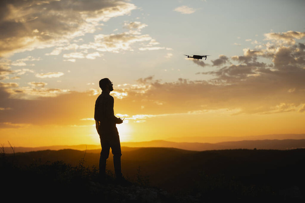 Silhouette di un uomo con pilotaggio di un drone in ambiente rurale durante il tramonto - Foto, immagini