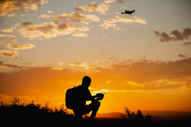 Silhouette eines Mannes, der bei Sonnenuntergang eine Drohne in den ländlichen Raum steuert - Foto, Bild