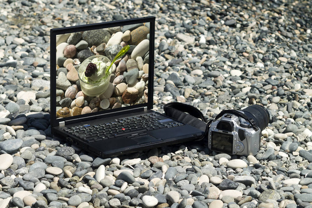 Ordenador portátil con imagen de helado en su monitor y cámara colocada entre guijarros grises en la playa de mar - Foto, Imagen