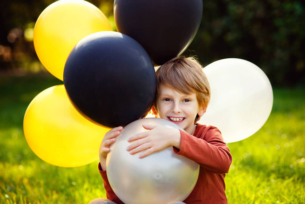 Jeune garçon roux jouant avec un tas de ballons jaunes blancs noirs dans le parc. - Photo, image