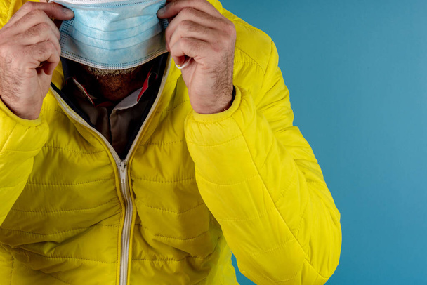 黄色のジャケットの男は青の背景にコロナウイルスに対する保護マスクを使用しています,高いアラートと病気に対する戦い, COVID-19, SARSのCoV,ウイルス2020 - 写真・画像