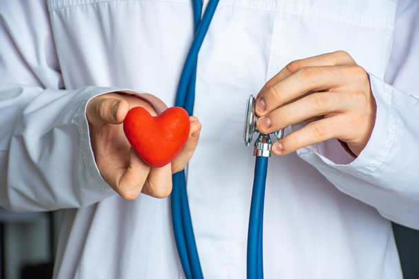 Un medico o un operatore sanitario mantiene la forma del cuore in una mano e lo stetoscopio nell'altra. Concetto fotografico per diagnosticare e determinare le cause dell'insorgenza di malattie cardiache e cardiovascolari - Foto, immagini