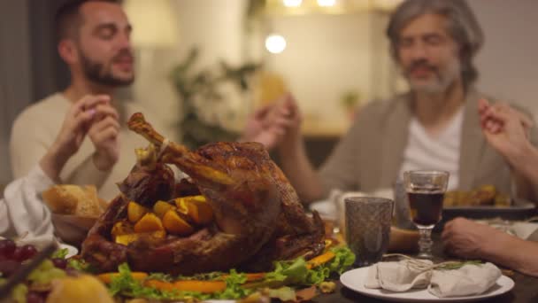 ローストターキーは感謝祭の日に神に祈る夕食のテーブルに一緒に座っている4人の白人のショット映像を焦点を当てた - 映像、動画
