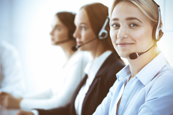 Call center and business people concept. Beautiful business woman with headphones consulting clients. Group of diverse phone operators at work in office - Foto, Imagen