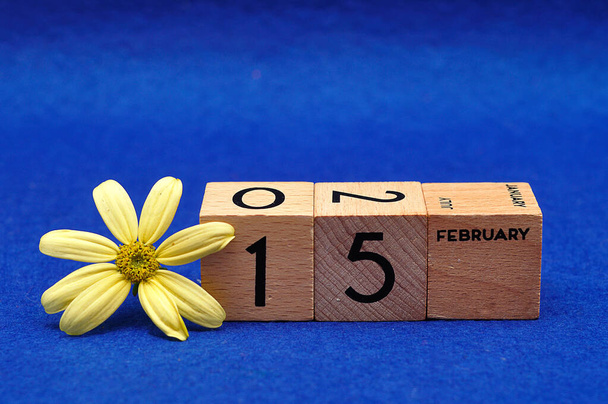 15 lutego na drewnianych blokach z żółtym kwiatem na niebieskim tle - Zdjęcie, obraz