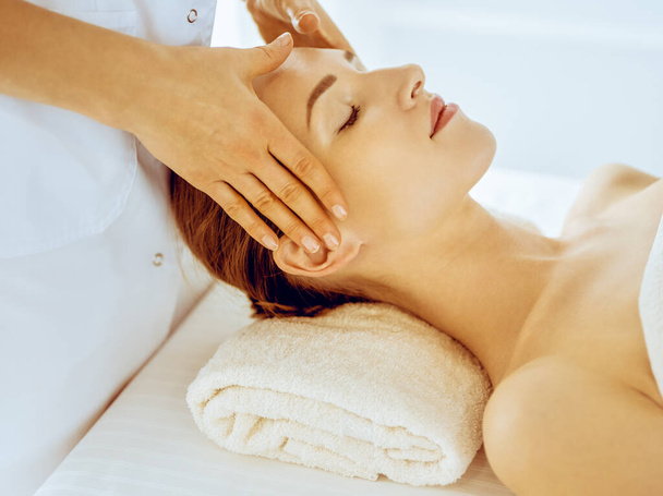 Beautiful woman enjoying facial massage with closed eyes in spa center. Relax treatment concept in medicine - Foto, imagen