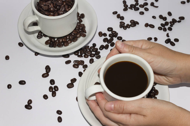 Kobiece ręce trzymające filiżankę czarnej kawy z ziarnami kawy.Białe tło. - Zdjęcie, obraz