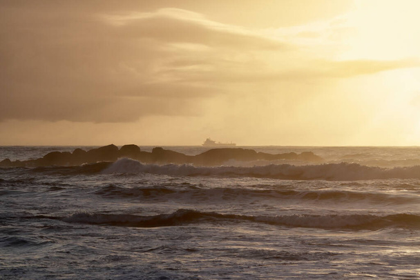 Ropný tanker na obzoru křižující skalnaté severní pobřeží Portugalska při západu slunce - Fotografie, Obrázek