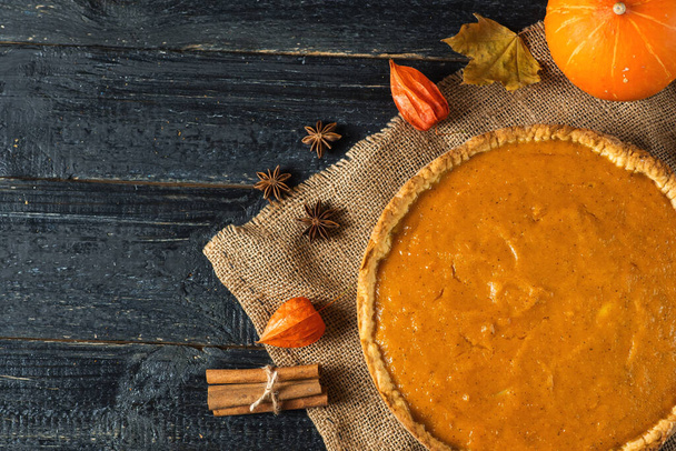Pumpkin pie on a wooden table with ingredients and decor - Фото, изображение