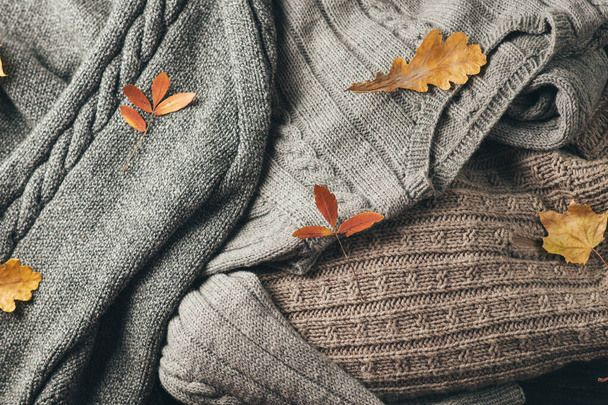Arkaplanda kalın kazaklar var. Elle örülmüş kıyafetlerin üst görünüşü sonbahar kuru yapraklarıyla - Fotoğraf, Görsel