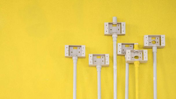 Boîtes de prises électriques en plastique avec tuyaux en PVC pour l'installation d'un système électrique sur fond de mur de ciment jaune à l'intérieur du chantier de construction de la maison  - Photo, image