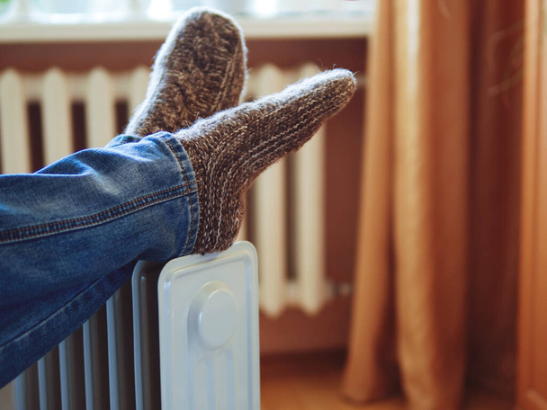 Feet in warm knitted socks on the heater. Heating season - Photo, Image