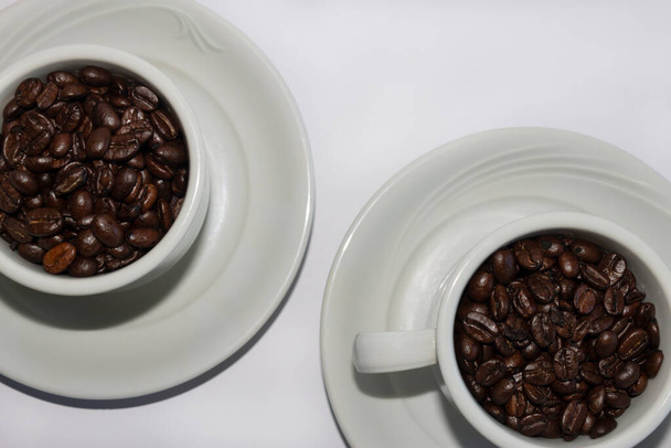 Кавові зерна в двох чашках кави, на білому ізольованому фоні. Вид зверху. Макро
. - Фото, зображення